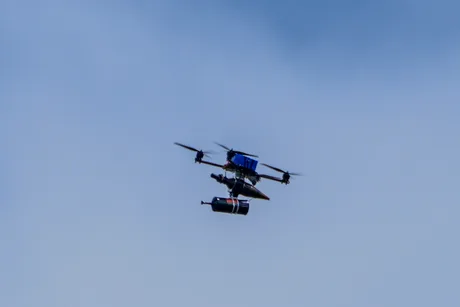 Dronă echipată cu explozibil zburând pe un fundal albastru.